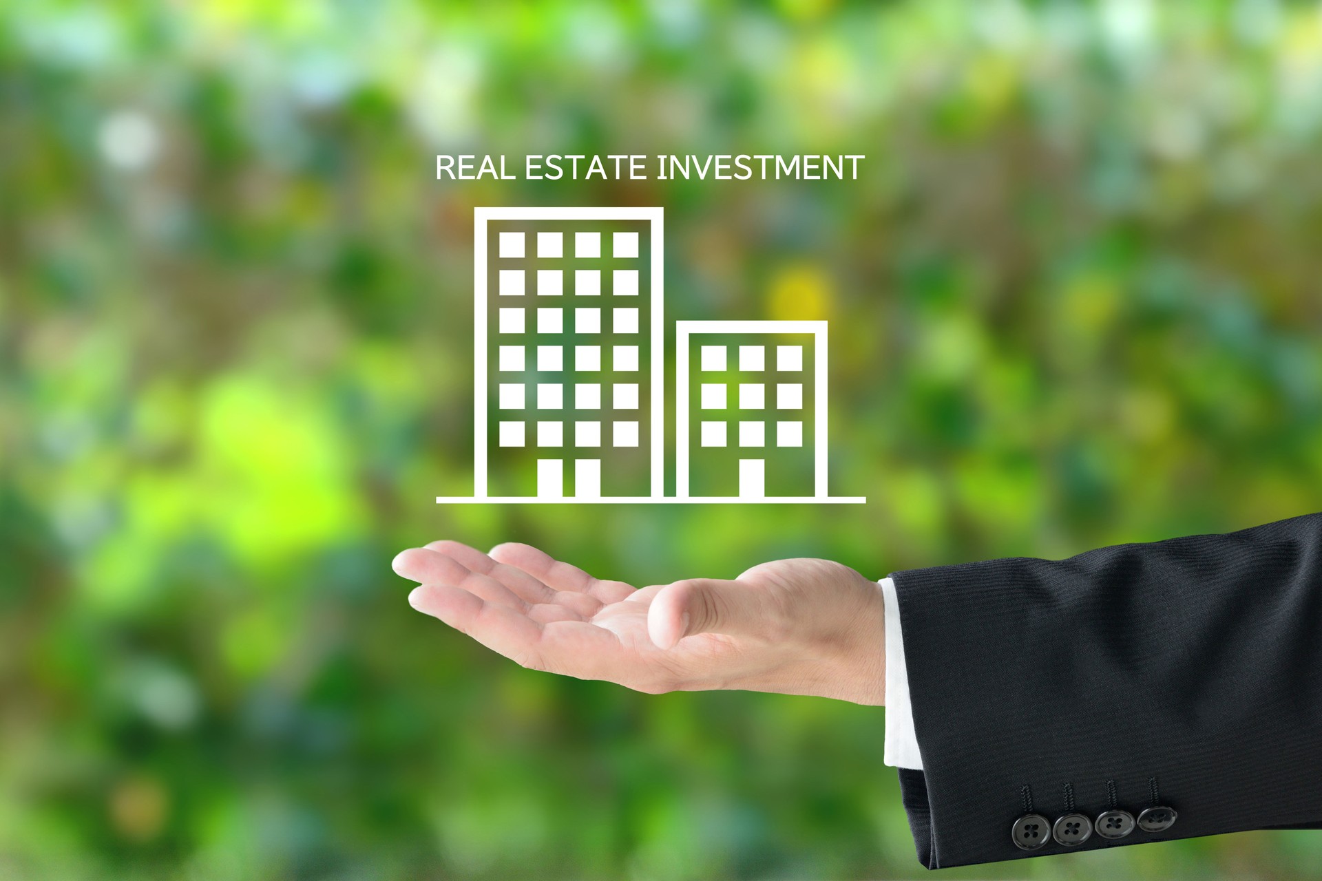 Business man's hand and building pictogram with REAL ESTATE INVESTMENT word